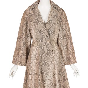 Peut inclure: Manteau vintage à motif peau de serpent, présenté sur un mannequin. Le manteau a un col cranté, des manches longues et une fermeture boutonnée. La palette de couleurs comprend des nuances de beige, de marron et de gris, créant un aspect texturé.