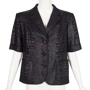 May include: Black short-sleeve blazer with a textured pattern. The blazer features a notched collar, two front pockets, and three brown buttons. The garment is displayed on a white mannequin.