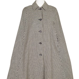 Peut inclure: Un manteau cape à motif pied-de-poule noir et beige, boutonné sur le devant. Le manteau est présenté sur un mannequin avec une tête et des jambes blanches.
