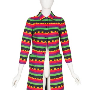 May include: A knee-length coat featuring a vibrant horizontal striped pattern in shades of black, bright green, purple, and yellow. The coat has a classic collar, three-quarter length sleeves, a front button closure, and two rectangular patch pockets.
