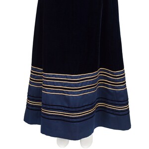 Puede incluir: Falda larga de terciopelo azul marino con una cinturilla ancha azul marino. El dobladillo presenta rayas horizontales en azul marino, dorado y negro. La falda es de diseño clásico y elegante.