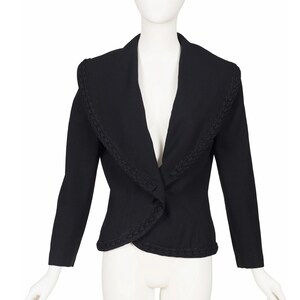 May include: A black jacket with a wide, decorative collar and long sleeves. The jacket has a single button closure and a tailored fit. The collar and edges are trimmed with a textured design. The jacket is displayed on a mannequin.