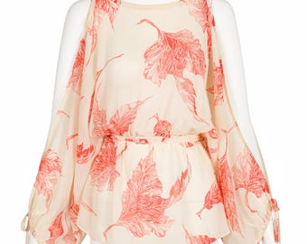 May include: A cream-colored blouse with a red leaf pattern. The blouse features long, flowing sleeves and a cinched waist. The sleeves are tied at the shoulders and wrists. The blouse is displayed on a mannequin.