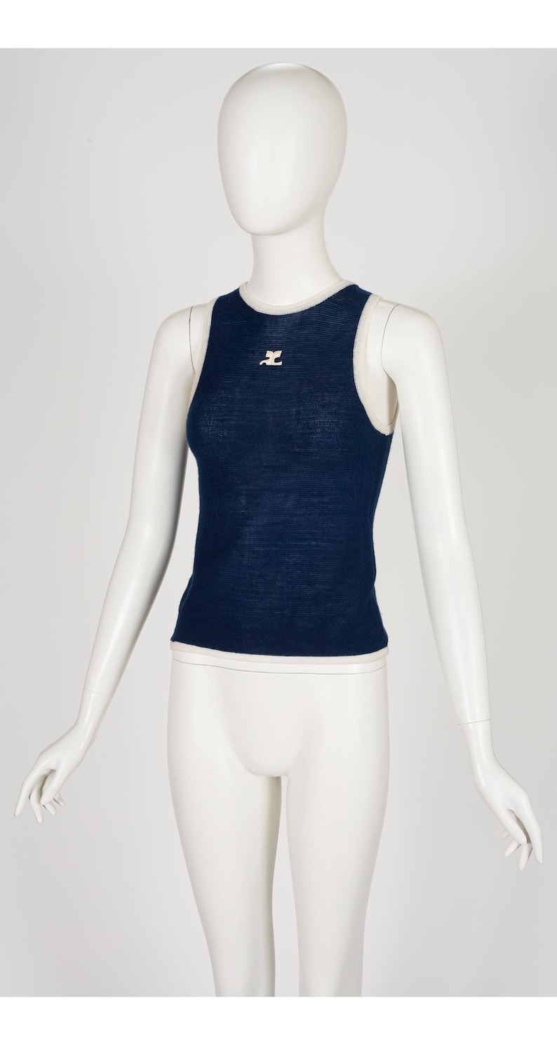 Peut inclure: Un d&eacute;bardeur bleu marine avec une bordure blanche et un petit logo rose sur la poitrine. Le haut sans manches est pr&eacute;sent&eacute; sur un mannequin. Le haut est en tissu tricot&eacute;.