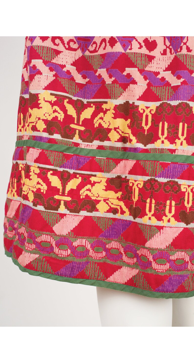 May include: A red skirt with a colorful geometric pattern. The pattern features a variety of shapes and colors, including pink, yellow, green, and purple.
