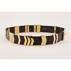 May include: A black leather belt with gold-colored metal accents. The belt features a series of gold rectangular and arrow-shaped embellishments. The belt is approximately 32 inches in length.