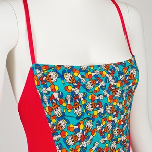 May include: Red and turquoise swimsuit with a pattern of Donald Duck holding balloons. The text "Walt Disney Productions" is visible on the fabric.