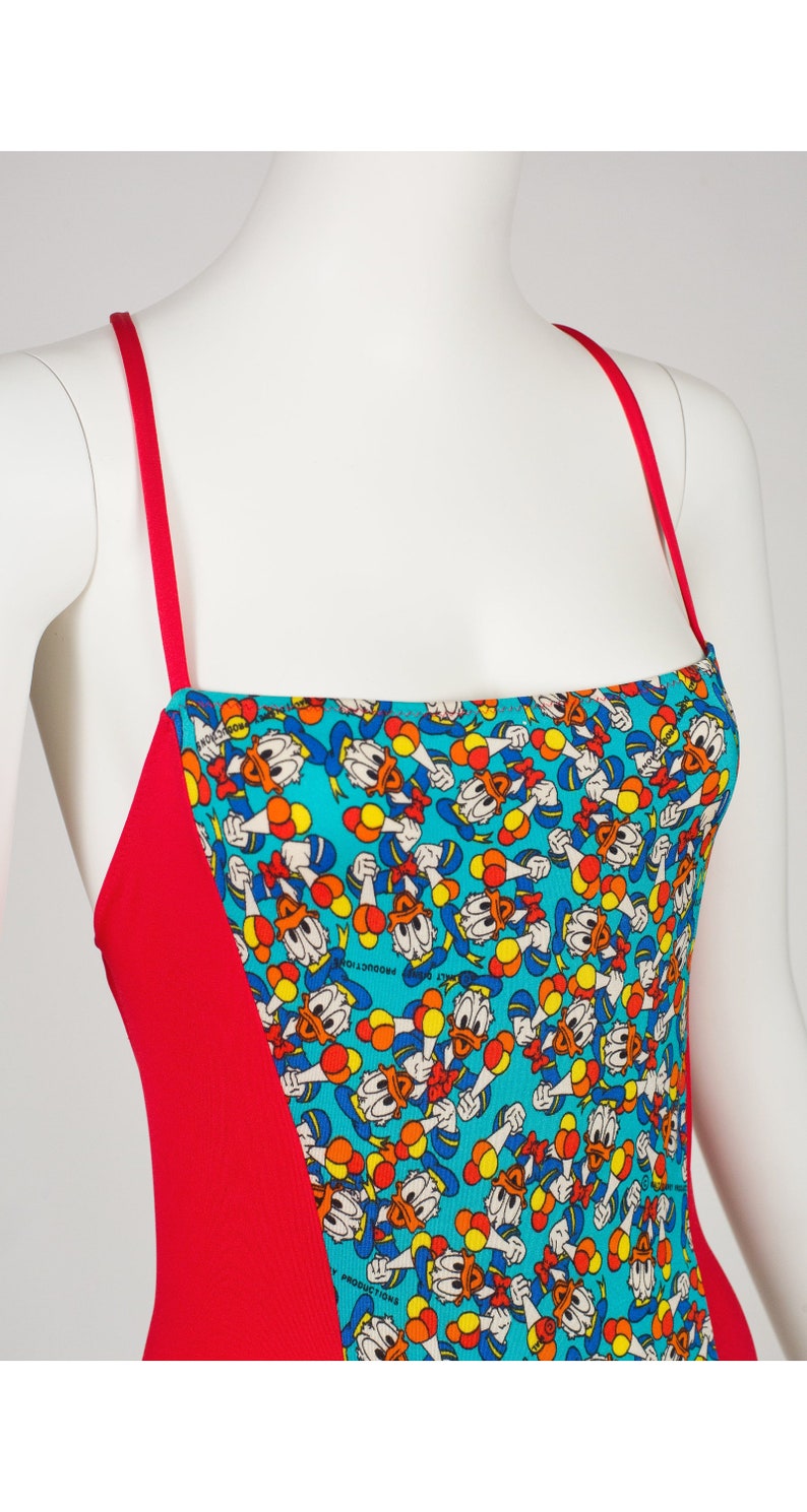 May include: Red and turquoise swimsuit with a pattern of Donald Duck holding balloons. The text "Walt Disney Productions" is visible on the fabric.
