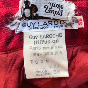 May include: A white tag with black text that reads "Guy Laroche Diffusion Paris Made in France Size 6 - Taille 36 T 5 2 9 Color Coloris 36" attached to a red fabric.
