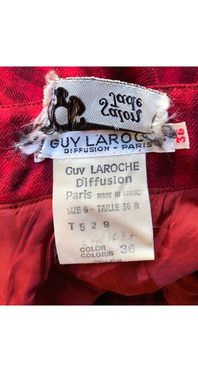 May include: A white tag with black text that reads "Guy Laroche Diffusion Paris Made in France Size 6 - Taille 36 T 5 2 9 Color Coloris 36" attached to a red fabric.