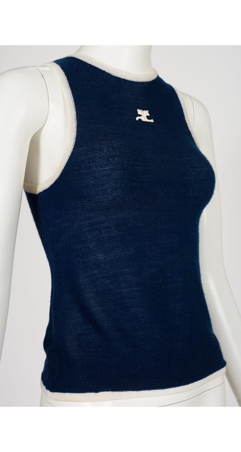 Peut inclure: Un d&eacute;bardeur bleu marine avec une bordure blanche autour de l'encolure et des emmanchures. Un petit embl&egrave;me blanc est centr&eacute; sur la poitrine. Le haut est pr&eacute;sent&eacute; sur un mannequin.