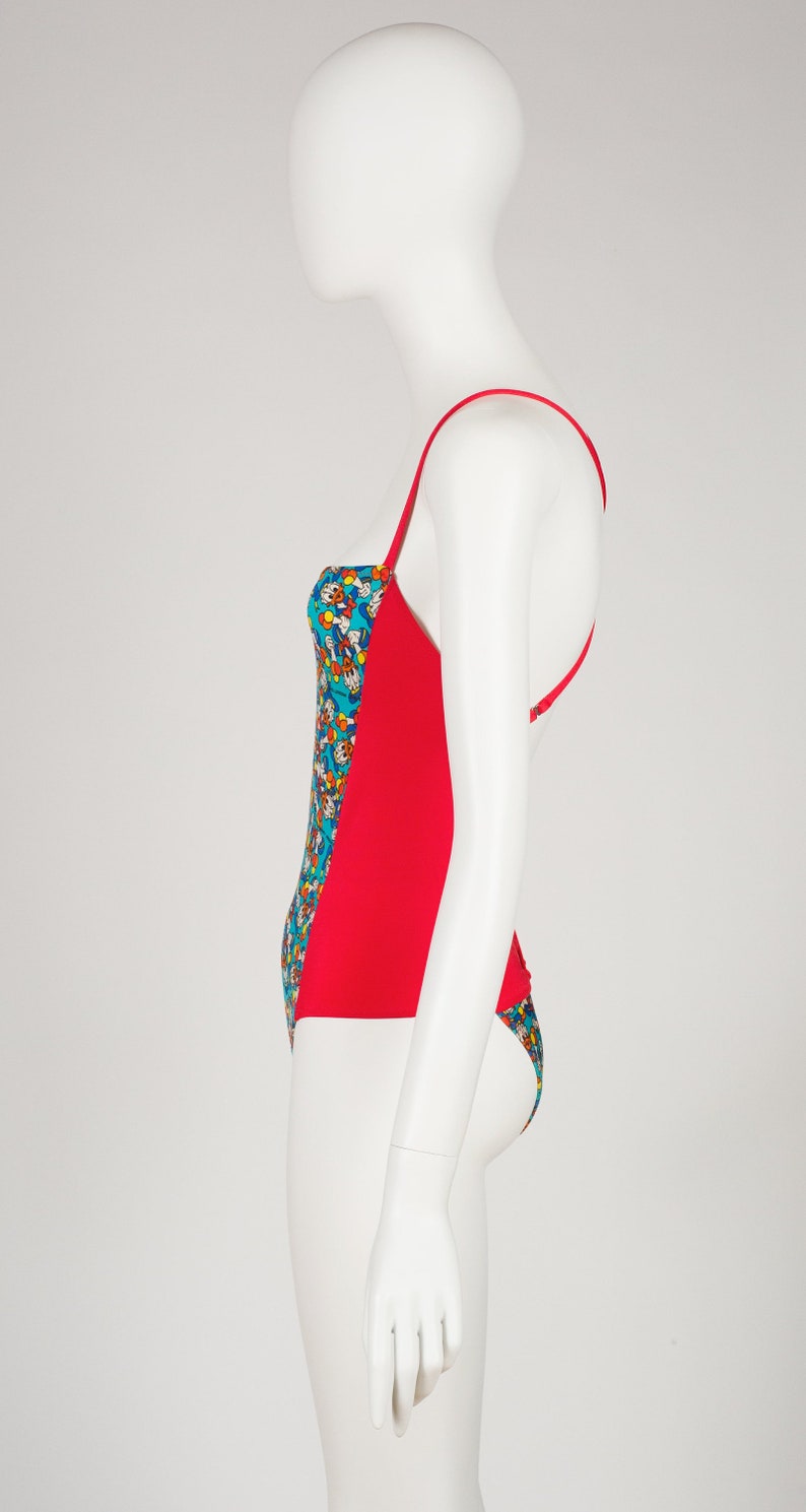 May include: A red and blue swimsuit with a colorful cartoon print. The swimsuit has a halter top and a low back.