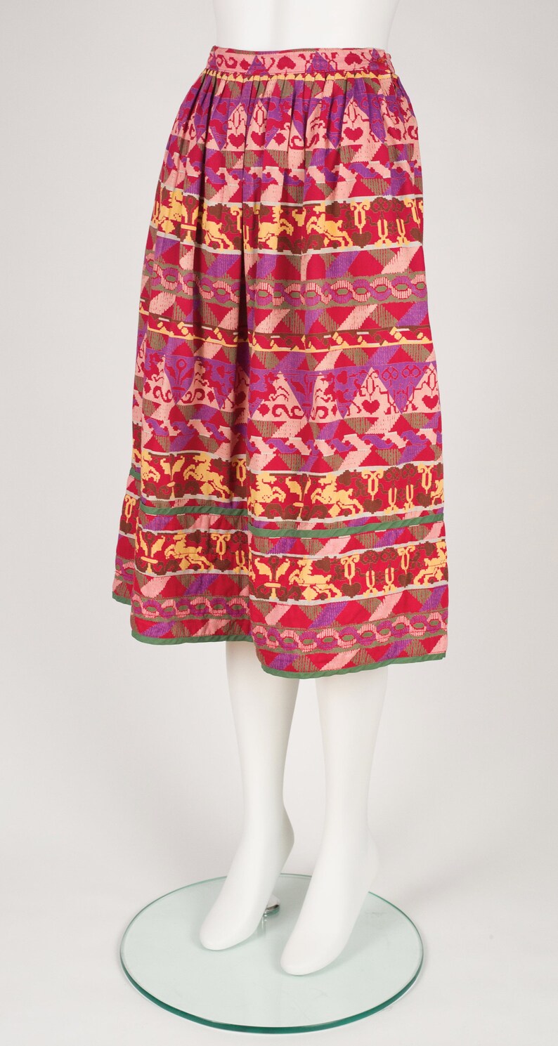 May include: A colorful midi skirt with a geometric pattern in shades of pink, red, yellow, and green. The skirt has a gathered waistband and a flowing silhouette.