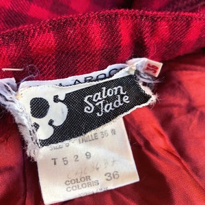 May include: A white tag with black text that reads "Salon Jade" and size information. The tag is attached to a red and black plaid fabric.