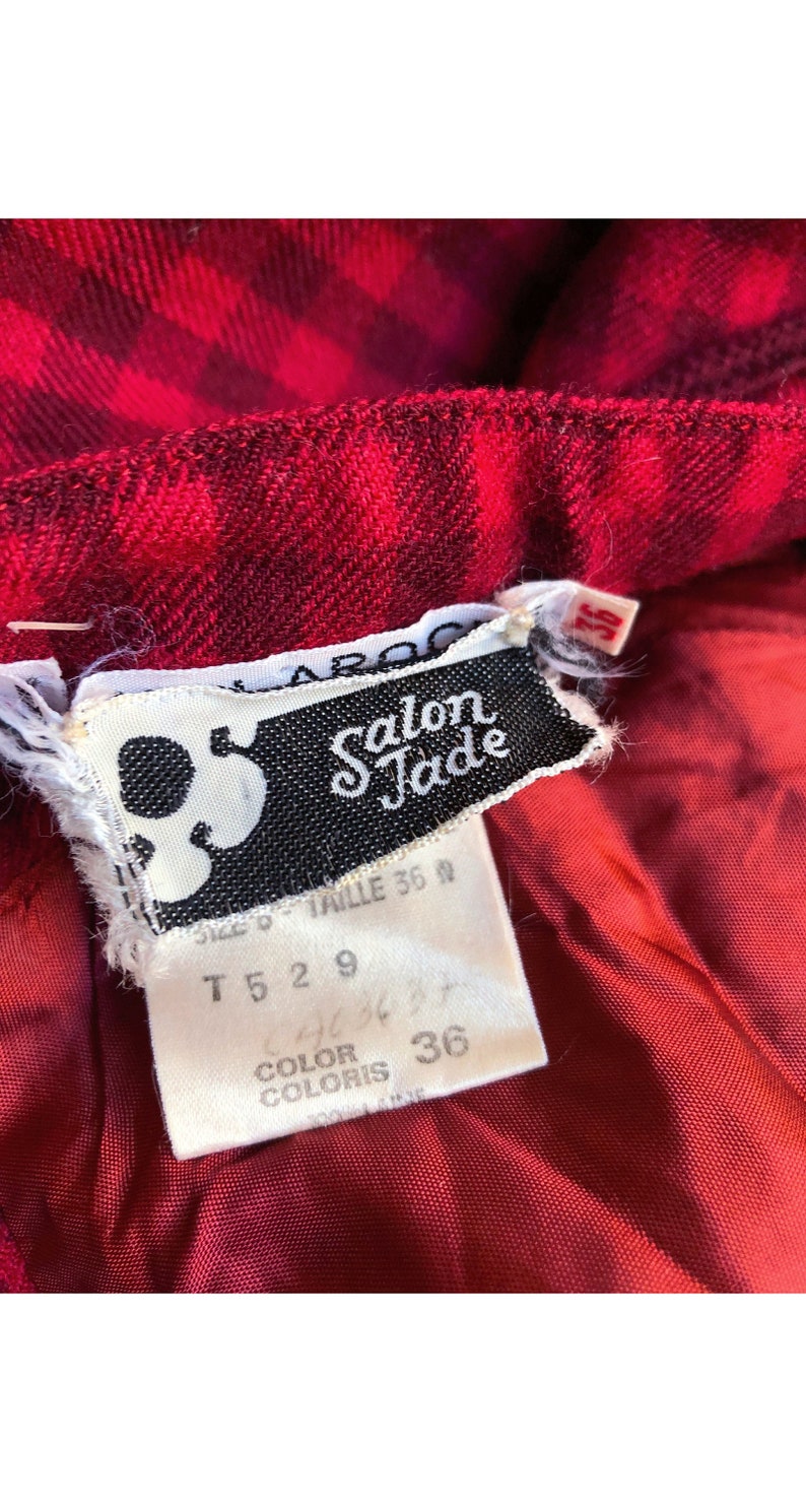 May include: A white tag with black text that reads "Salon Jade" and size information. The tag is attached to a red and black plaid fabric.