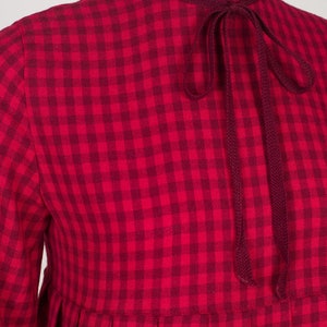 May include: A red and white gingham dress with a long sleeve and a tie at the neck.
