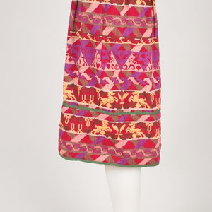 May include: A red, pink, purple, and yellow patterned skirt with a green trim. The skirt is pleated and has a geometric design.