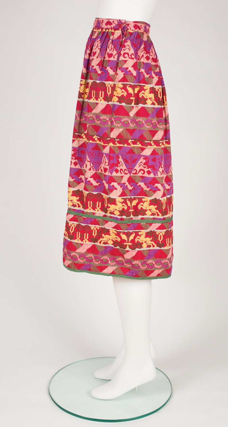 May include: A red, pink, purple, and yellow patterned skirt with a green trim. The skirt is pleated and has a geometric design.