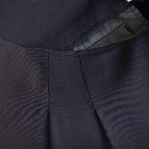 以下が含まれることがあります： ネイビーブルーの衣服のクローズアップ。おそらくジャケットまたはコートで、襟とラペル部分を示しています。生地は微妙なリブのテクスチャを持っています。縫い目は縫い目に沿って見え、仕立てのディテールを強調しています。