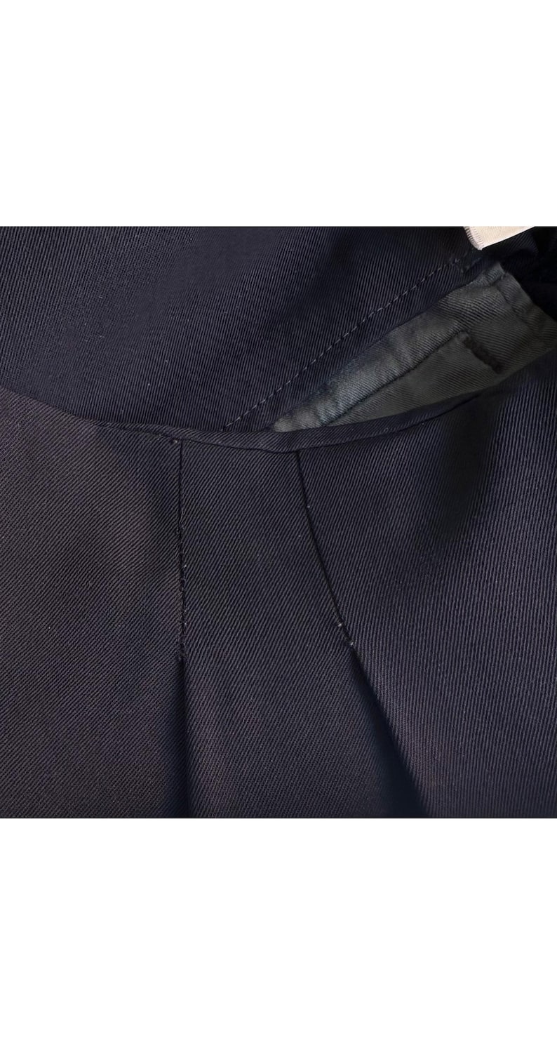 以下が含まれることがあります： ネイビーブルーの衣服のクローズアップ。おそらくジャケットまたはコートで、襟とラペル部分を示しています。生地は微妙なリブのテクスチャを持っています。縫い目は縫い目に沿って見え、仕立てのディテールを強調しています。