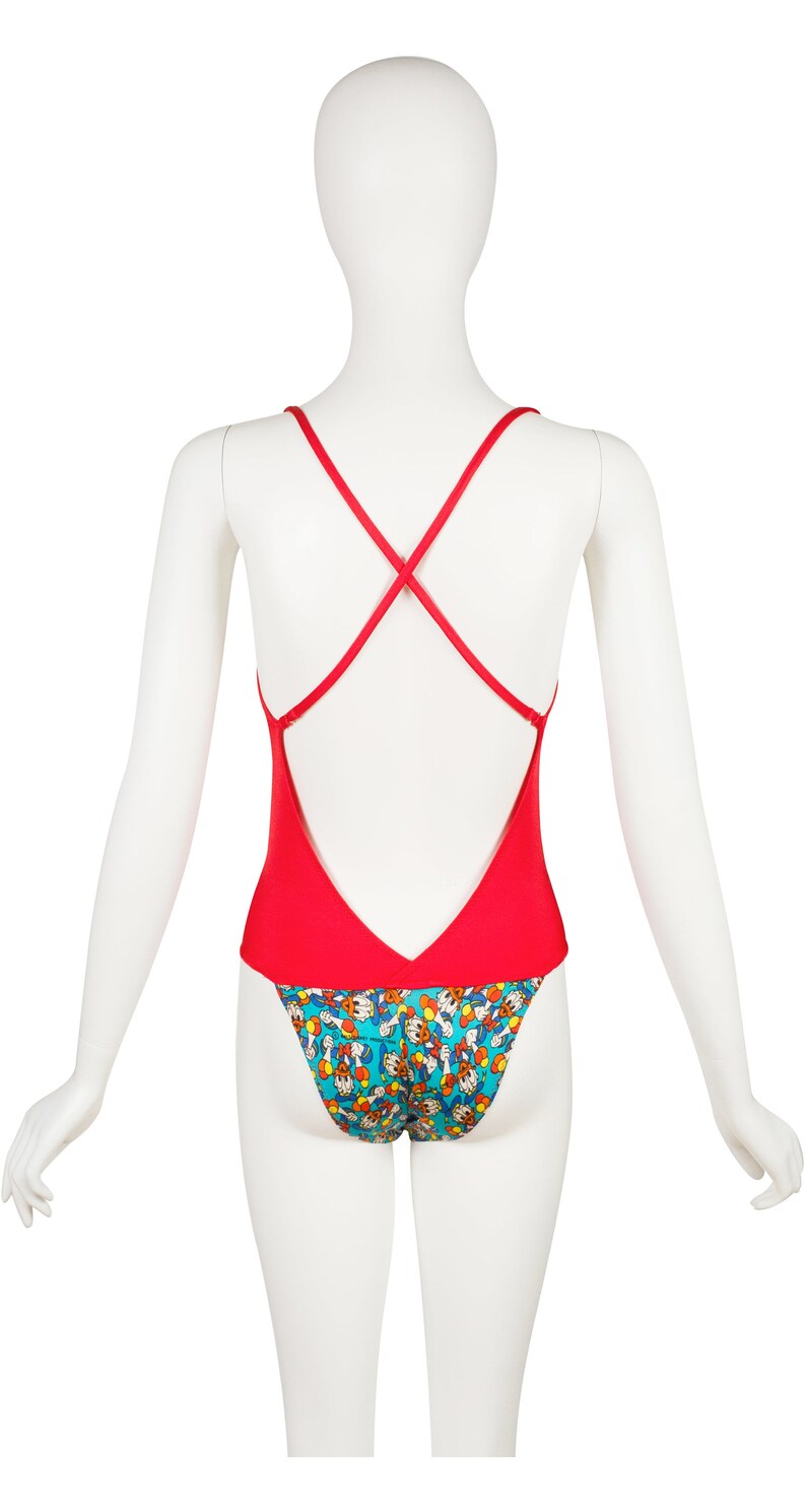 May include: Red swimsuit with a criss-cross back strap and a blue and yellow print of cartoon characters on the bottom.