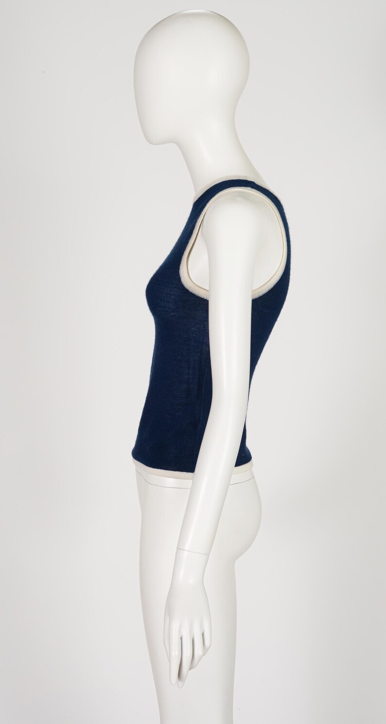Peut inclure: Un d&eacute;bardeur bleu marine avec une bordure cr&egrave;me. Le haut sans manches est pr&eacute;sent&eacute; sur un mannequin, mettant en valeur sa coupe ajust&eacute;e. La bordure est visible autour de l'encolure et des emmanchures.