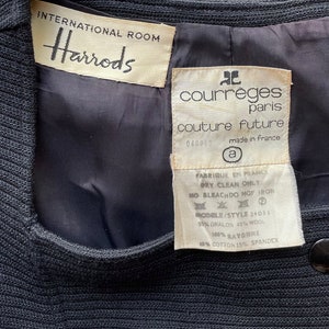Op de afbeelding: Een zwarte blazer met een wit label met de tekst "International Room Harrods" en een wit label met de tekst "courr&egrave;ges paris couture future 040863 made in france" en wasinstructies.