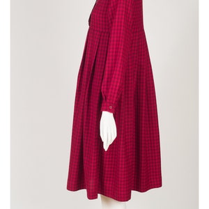 May include: A red and black gingham dress with a high neck and long sleeves. The dress has a gathered skirt and a bow at the neck.