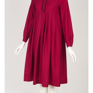 May include: A red and black gingham dress with a high neck and long sleeves. The dress has a bow at the neck and a gathered skirt.