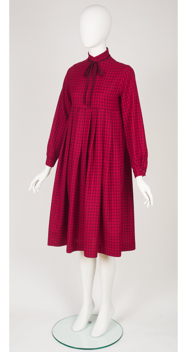 May include: A red and black gingham dress with a high neck and long sleeves. The dress has a bow at the neck and a gathered skirt.