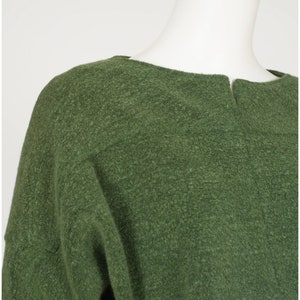Puede incluir: Un su&eacute;ter verde con cuello redondo y mangas largas. El su&eacute;ter est&aacute; hecho de un material suave y peludo.