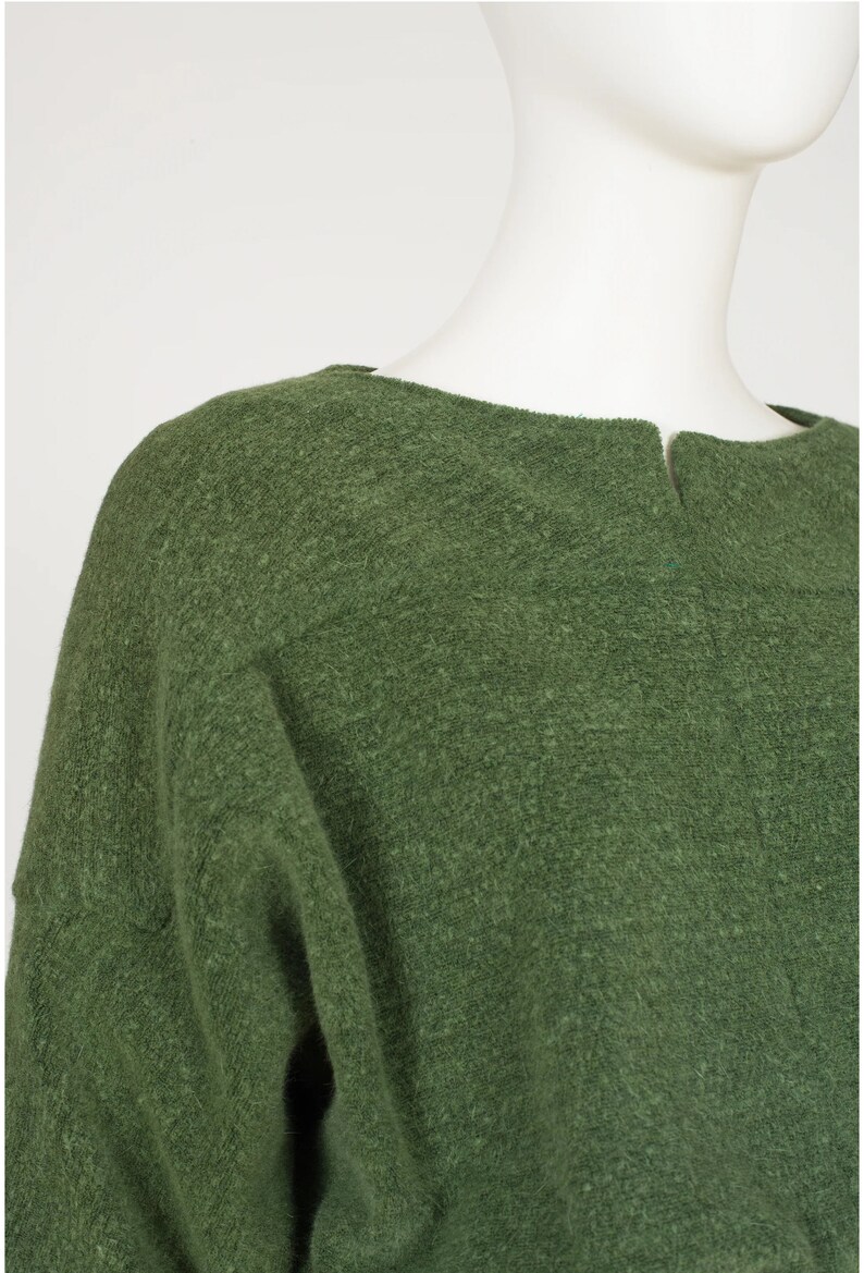 Puede incluir: Un su&eacute;ter verde con cuello redondo y mangas largas. El su&eacute;ter est&aacute; hecho de un material suave y peludo.