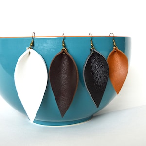 May include: Four pairs of leather earrings in a teal bowl. The earrings are shaped like teardrops and are in white, brown, black, and tan.