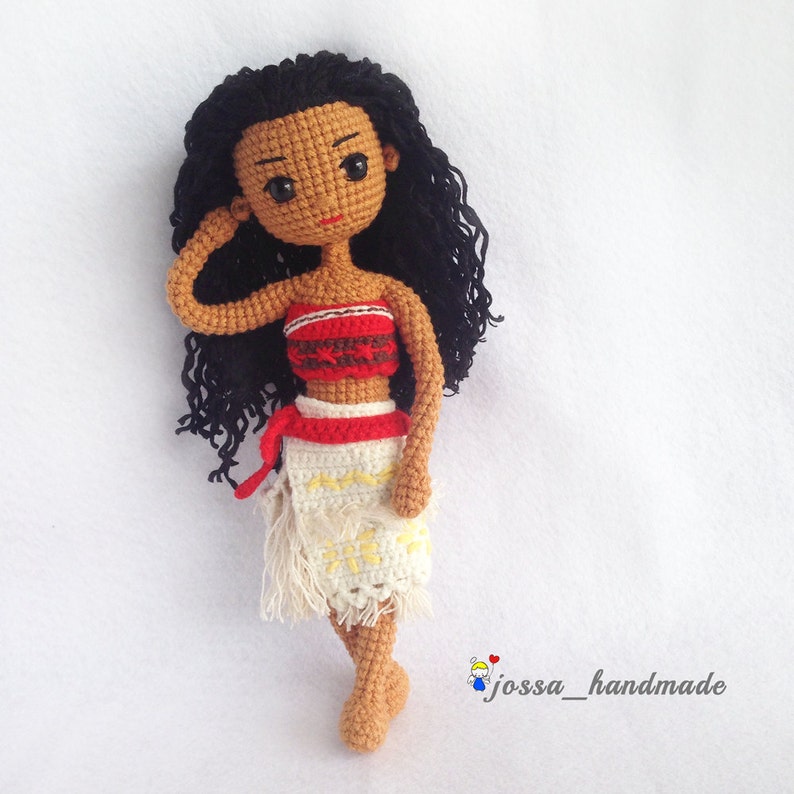 May include: Crocheted doll with brown skin, black curly hair, and a red and white top. The doll is wearing a white skirt with a yellow flower design and is standing on a white background. The text "jossa_handmade" is visible in the bottom right corner of the image.