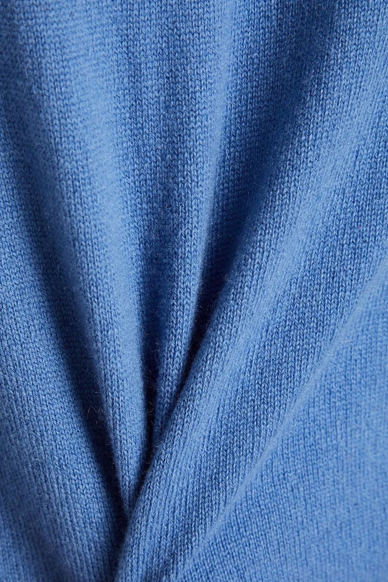 以下が含まれることがあります： 柔らかな青いニット生地のクローズアップ。生地は細かい編み目で、わずかに質感のある表面をしています。