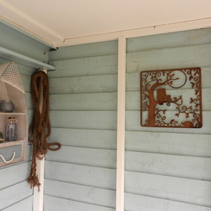 May include: A light blue wooden wall with a white trim. A small wooden boat shelf with a net and jars is on the left side of the wall. A rusty metal owl and tree wall decor is on the right side of the wall.
