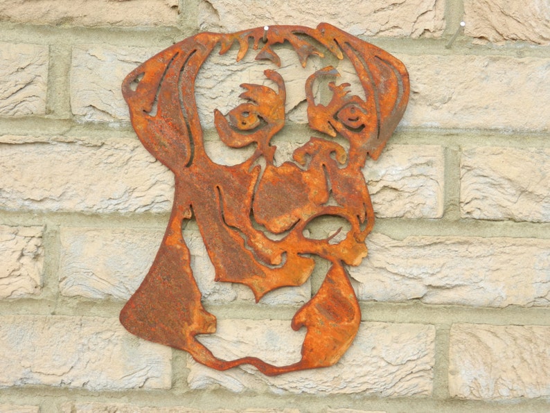 K&ouml;nnte beinhalten: Ein rostiger Metallausschnitt eines Boxerkopfes, der an einer Backsteinwand montiert ist. Der Ausschnitt ist eine Silhouette des Hundekopfes mit Details von Augen, Nase und Maul.