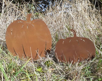 Könnte beinhalten: Zwei rostige Metall-Kürbis-Silhouetten in einem Feld mit hohem Gras. Der größere Kürbis befindet sich im Vordergrund und der kleinere Kürbis dahinter.