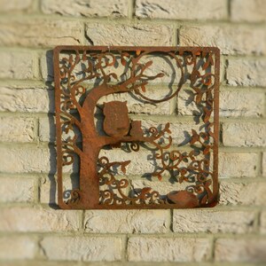 May include: Rustic metal wall art featuring a tree with two owls perched on branches. The tree is intricately cut with a leafy design and a full moon in the background. The metal has a rusty brown finish.