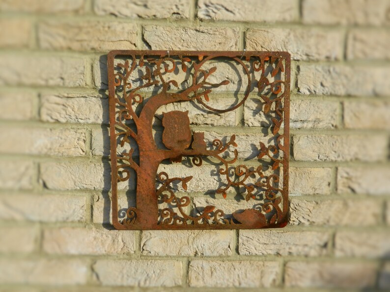 May include: Rustic metal wall art featuring a tree with two owls perched on branches. The tree is intricately cut with a leafy design and a full moon in the background. The metal has a rusty brown finish.