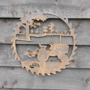Puede incluir: Una hoja de sierra de metal oxidada con un dise&ntilde;o recortado de un tractor conduciendo por un bosque. El tractor tiene un arado unido al frente.