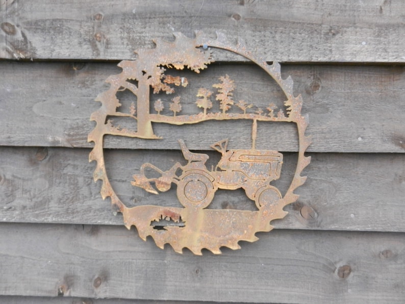Puede incluir: Una hoja de sierra de metal oxidada con un dise&ntilde;o recortado de un tractor conduciendo por un bosque. El tractor tiene un arado unido al frente.