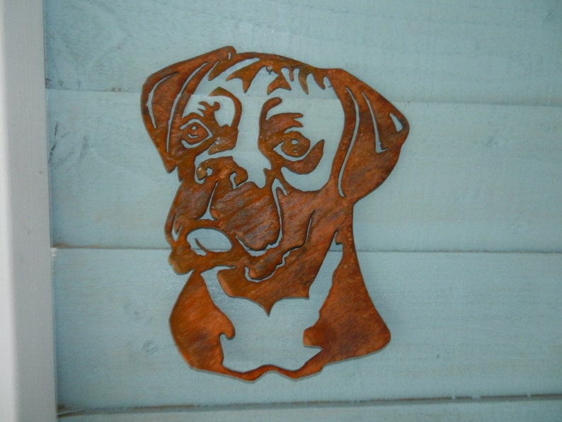 K&ouml;nnte beinhalten: Ein rostiger Metallausschnitt eines Boxerkopfes. Der Ausschnitt ist eine Silhouette des Hundekopfes mit einem detaillierten Gesicht und Ohren.