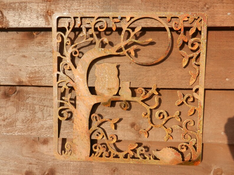 May include: Rustic metal wall art featuring a tree with two owls perched on branches. The tree is intricately designed with swirling branches and leaves, creating a whimsical and nature-inspired design. The metal is a rusty brown color, adding to the rustic charm of the piece.