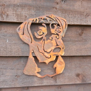 K&ouml;nnte beinhalten: Ein rostiger Metallausschnitt eines Hundekopfes in braunen und orangen Farbt&ouml;nen. Der Hundekopf ist nach vorne gerichtet, die Ohren stehen ab und der Mund ist leicht ge&ouml;ffnet. Der Ausschnitt ist auf einer Holzoberfl&auml;che montiert.