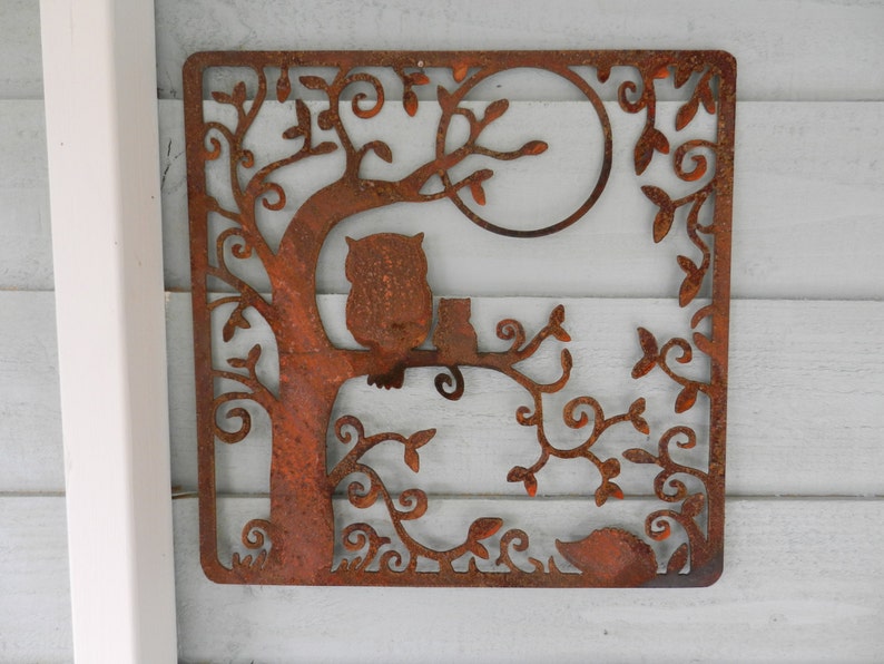 May include: Rustic metal wall art featuring a stylized tree with an owl and a cat perched on a branch. The design is cut out of metal and has a rusty brown finish.