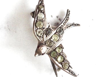 May include: A silver swallow brooch with clear and green rhinestones.