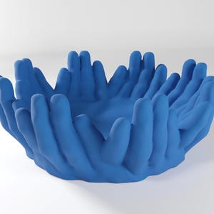 May include: A blue ceramic bowl shaped like a cluster of hands, with each finger forming a small cup. The bowl is perfect for holding small items like jewelry or keys.