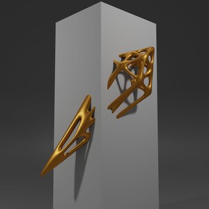 May include: Two gold-colored abstract sculptures mounted on a white wall. The sculptures are made of a smooth, organic material and have a flowing, asymmetrical design.