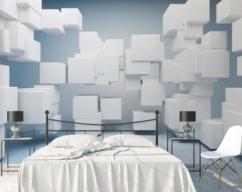 May include: A white bed with a white duvet cover and a black metal frame sits in front of a wall with a 3D geometric pattern of white cubes against a light blue background. Two black lamps with white shades are on black side tables next to the bed. A white chair with wooden legs is in the corner of the room.